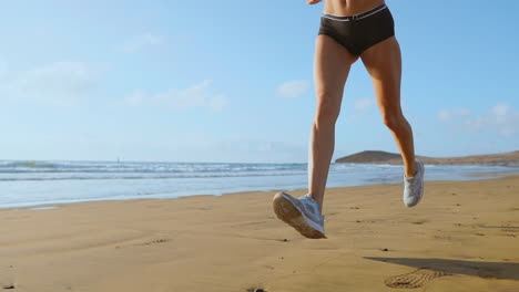 Beautiful-woman-in-sports-shorts-and-t-shirt-running-on-the-beach-with-white-sand-and-blue-ocean-water-on-the-island-in-slow-motion.-Waves-and-sand-hills-on-the-back-won